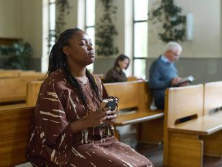 black woman sitting in a pew keeping her eyes closed