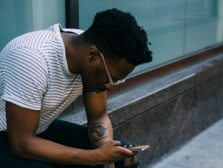 black man sitting down on a curb and looking at phone