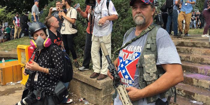 white supremacist standing with a large gun at a rally