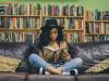 black woman sitting down crossed legged on a couch reading a book 